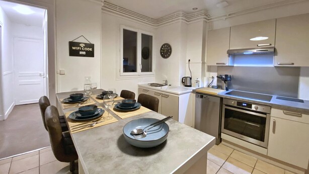Una cocina moderna con armarios blancos, horno integrado y comedor con mesa dispuesta para cuatro.