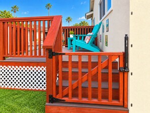 Eine Holzterrasse mit einer Treppe zu einem Balkon, einem türkisfarbenen Stuhl und einem weißen Gitterzaun.