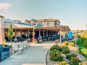 A hotel with a covered outdoor seating area, a pool, and a landscaped garden.