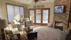A living room with a fireplace, a television mounted on the wall, and a large window with blinds. - Relaxing Getaway, Lakeside Sunsets, 6 Waterpark passes, Memories Galore!! (Arnolds Park)