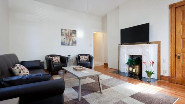 A living room with a sofa, two armchairs, a coffee table, a fireplace, and a television.