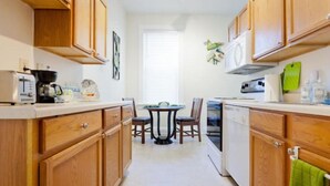 A kitchen with wooden cabinets, a dining table with chairs, a coffee maker, and a window with blinds.