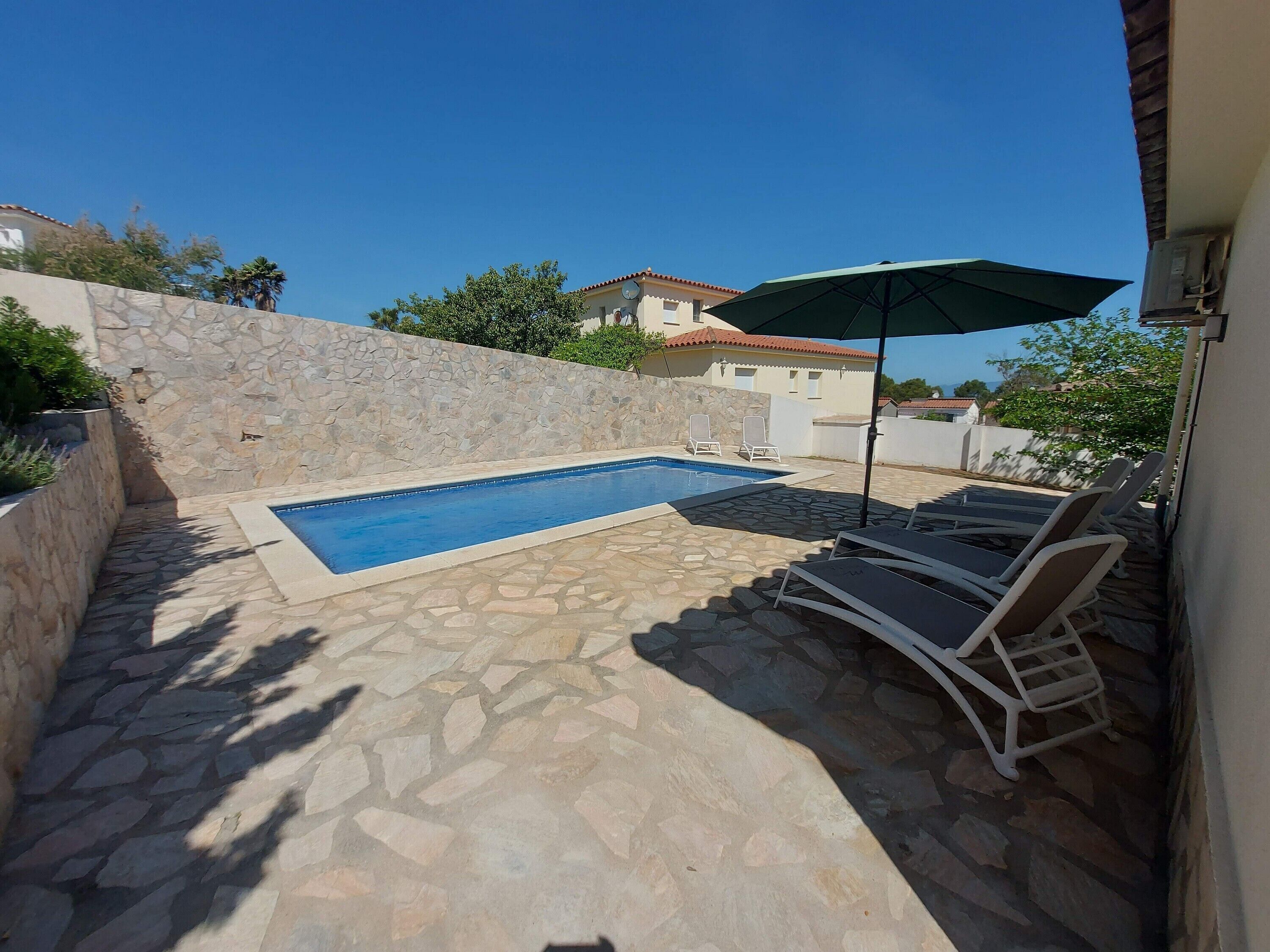 Una piscina con piastrelle in pietra, sdraio e un ombrellone.