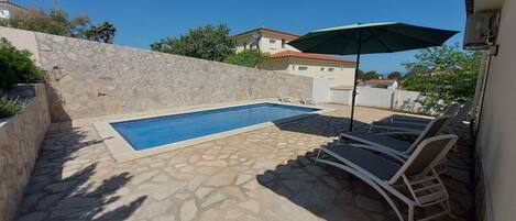 Una piscina con piastrelle in pietra, sdraio e un ombrellone.