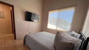 Ein Schlafzimmer mit einem Bett, einem an der Wand montierten Fernseher, einem Fenster mit Blick und einer Tür zu einem anderen Raum.