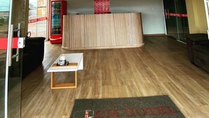 Un hall d'hôtel avec un plancher en bois, un comptoir d'accueil, une petite table avec une tasse et un paillasson portant le nom de l'hôtel.