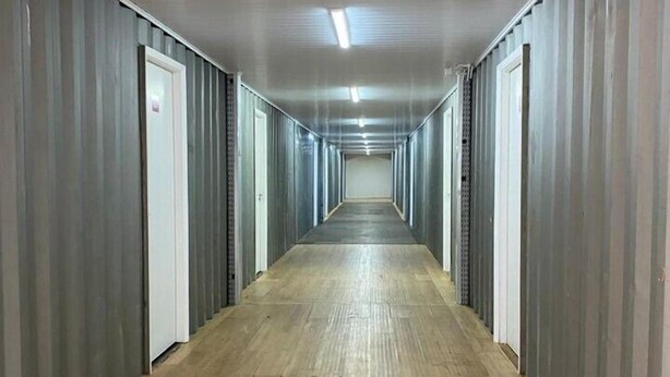 Un long couloir étroit aux murs métalliques et au plancher en bois, qui mène à plusieurs portes.