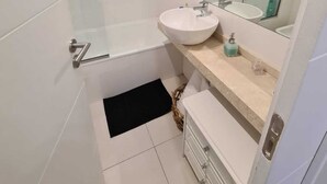 Et moderne badeværelse med et glas brusekabine, en hvid vask og et stort spejl over underskabet.