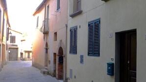 Une rue étroite, bordée de bâtiments des deux côtés, avec un mélange de façades en brique et en crépi, quelques fenêtres avec volets et une porte dont on peut clairement voir le numéro 14.