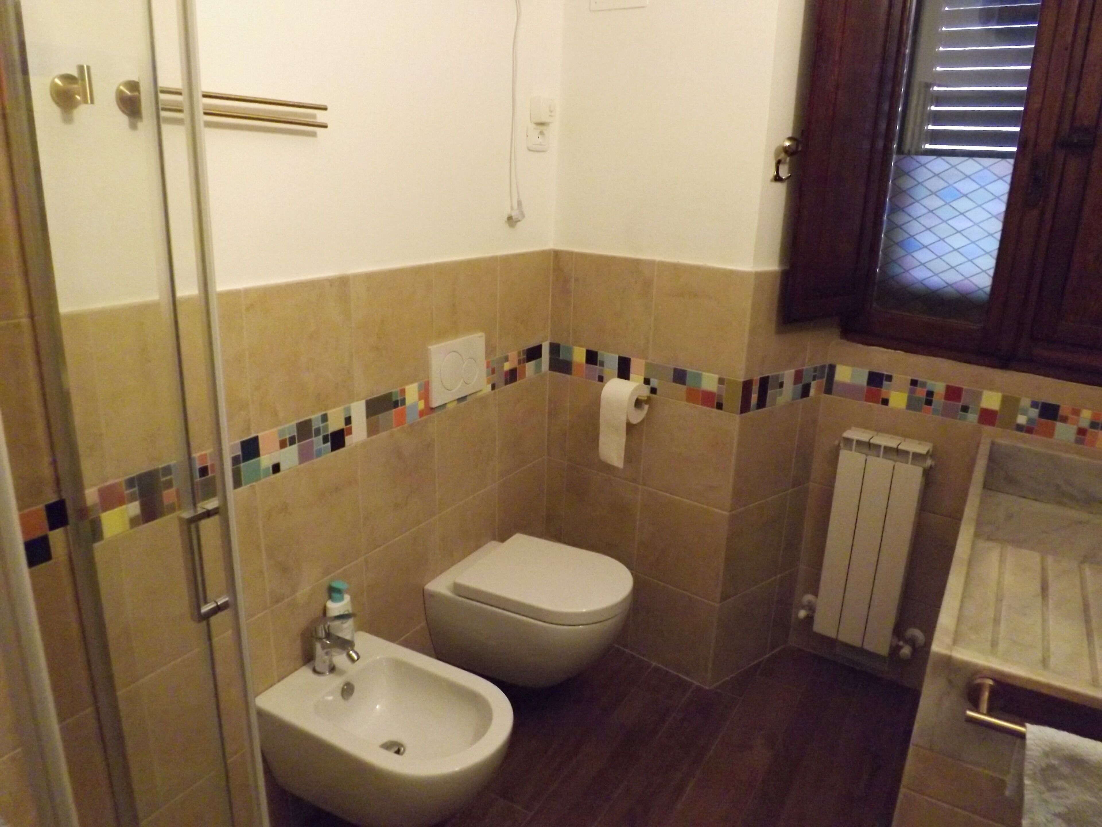 Une salle de bain équipée d’un bidet, de toilettes et d’une douche à parois de verre.