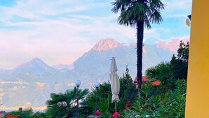 Ein Sitzbereich im Freien mit Stühlen und einem Tisch, umgeben von üppigem Grün und Blumen, mit Blick auf eine Berglandschaft.
