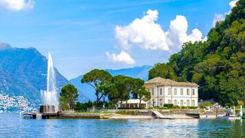 A waterfront property with a fountain, a large building, and a mountainous backdrop.