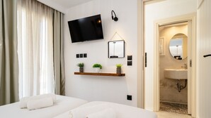 Habitación de hotel con dos camas, televisión, estante con plantas, espejo y baño visible a través de una puerta abierta.