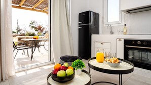 Cocina moderna con un refrigerador negro, un área de comedor con mesa y sillas, y una pequeña mesa redonda con un tazón de fruta y un vaso de jugo de naranja.