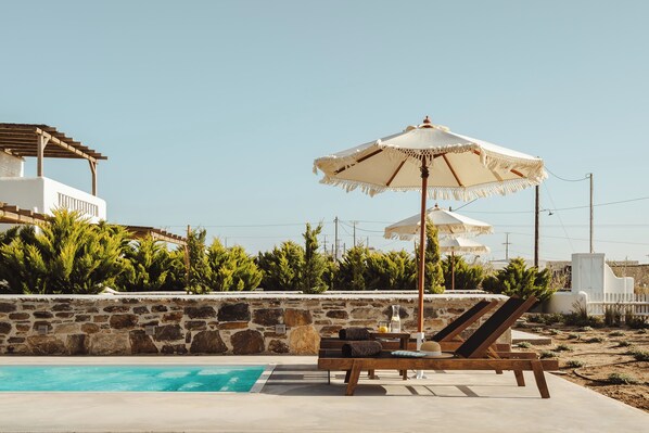 Ein Poolbereich mit Liegestühlen, Sonnenschirmen und einer Steinmauer.