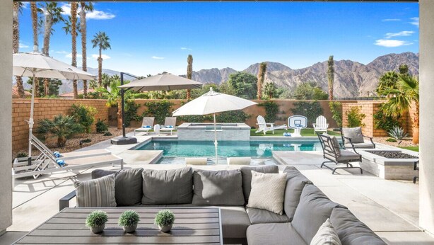 A pool area with lounge chairs and umbrellas, a sofa, and a view of mountains. - Signature View! Gorgeous BRAND NEW Home (Misters!) (La Quinta)