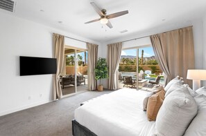 A hotel room with a large bed, a flat-screen TV, a ceiling fan, and a balcony with outdoor seating and a pool view. - Private pool & hot tub w/ mountain views (La Quinta)