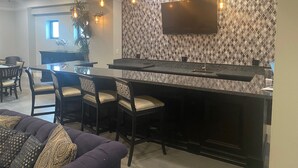 Ett modernt kök med en stor köksö, barstolar, hängande lampor och en platt-TV som är monterad på en vägg med ett mönstrat stänkskydd.