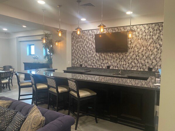 A modern kitchen with a large island, bar stools, pendant lighting, and a flat-screen TV mounted on a patterned backsplash. - Beachfront Resort-style Living! (Hollywood)