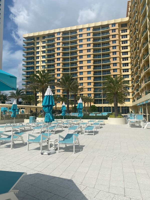 A hotel with a large outdoor pool area, multiple lounge chairs, and umbrellas.
