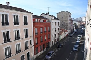 A street view of a residential area with multi-story buildings, parked cars, and a clear sky.
