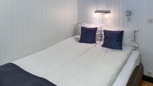 A single bed with white bedding and two dark pillows, a wall-mounted light fixture, and a power outlet on the wall. - Lovely apartment in Offersøy with sauna (Offersøy)