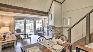 Un comedor con una mesa de madera dispuesta para cuatro personas, una chimenea de piedra y vistas al exterior a través de amplios ventanales.