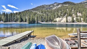 Una cabaña junto al lago con un muelle que se adentra en una masa de agua tranquila, rodeada de un bosque denso y montañas.