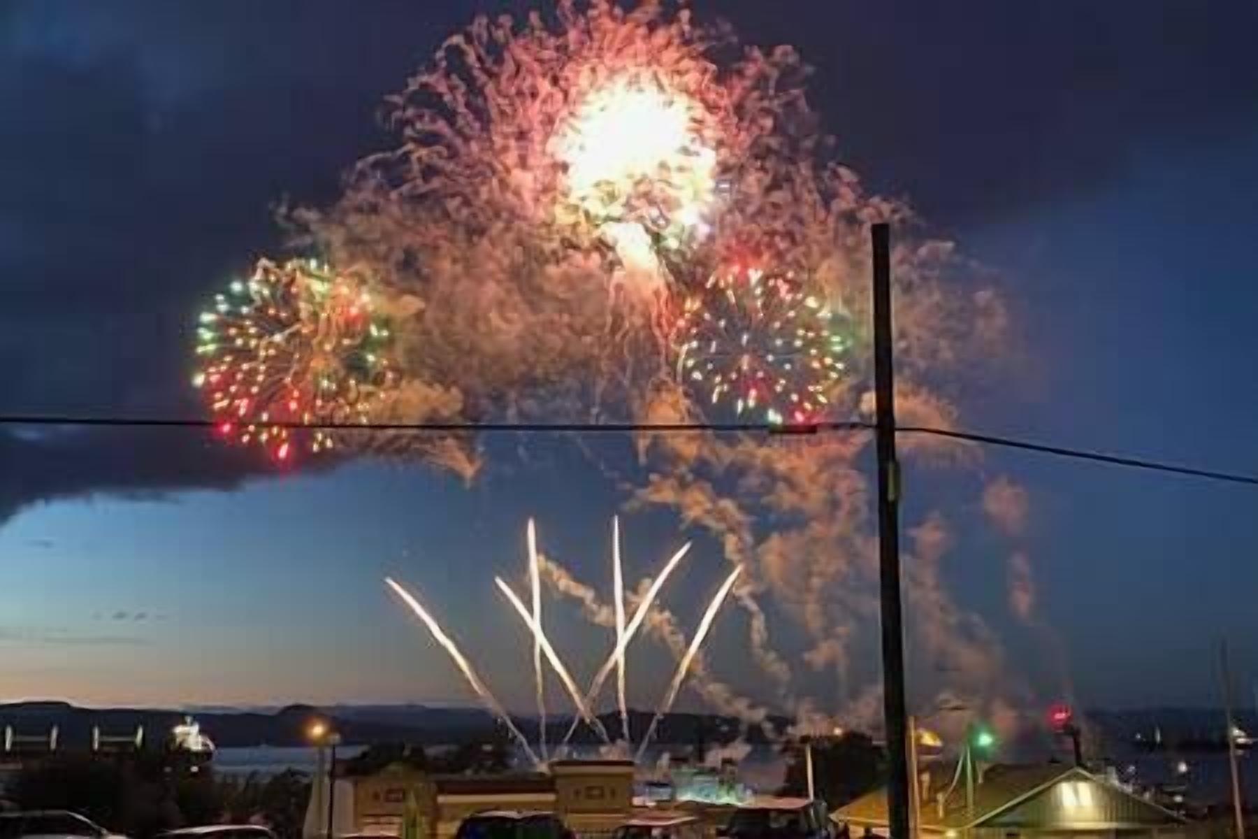 A fireworks display over a residential area with houses and a clear sky.