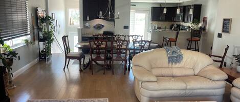 A spacious living room with a large beige sofa, a dining area with wooden chairs, and a kitchen in the background.