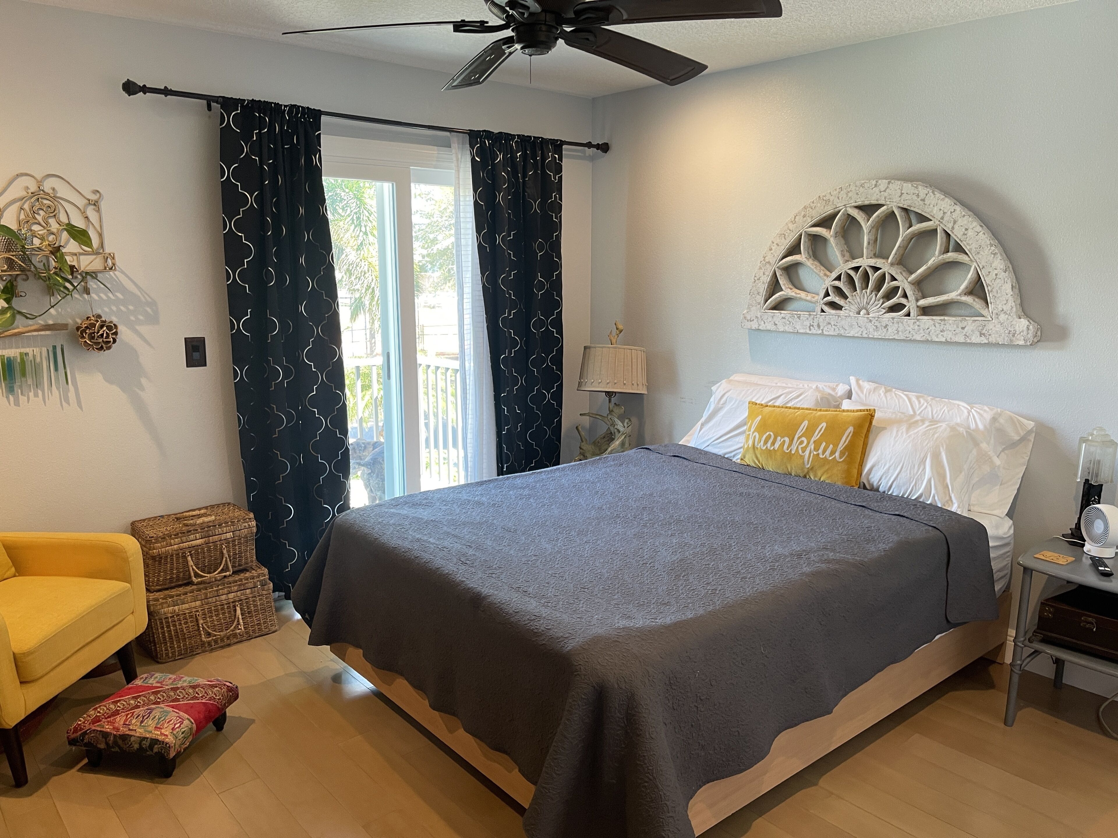 A bedroom with a bed, a chair, a lamp, a fan, and a decorative wall piece.