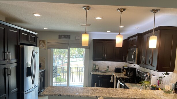 A modern kitchen with dark cabinets, a stainless steel refrigerator, a granite countertop, and pendant lighting. - One block from Beach. Spacious 2 bedroom apartment BTR #2197 (Indian Rocks Beach)