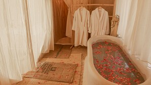 A bathroom with a bathtub filled with rose petals, wooden flooring, and white curtains. - Imperial Glory Lodges (Rissani)