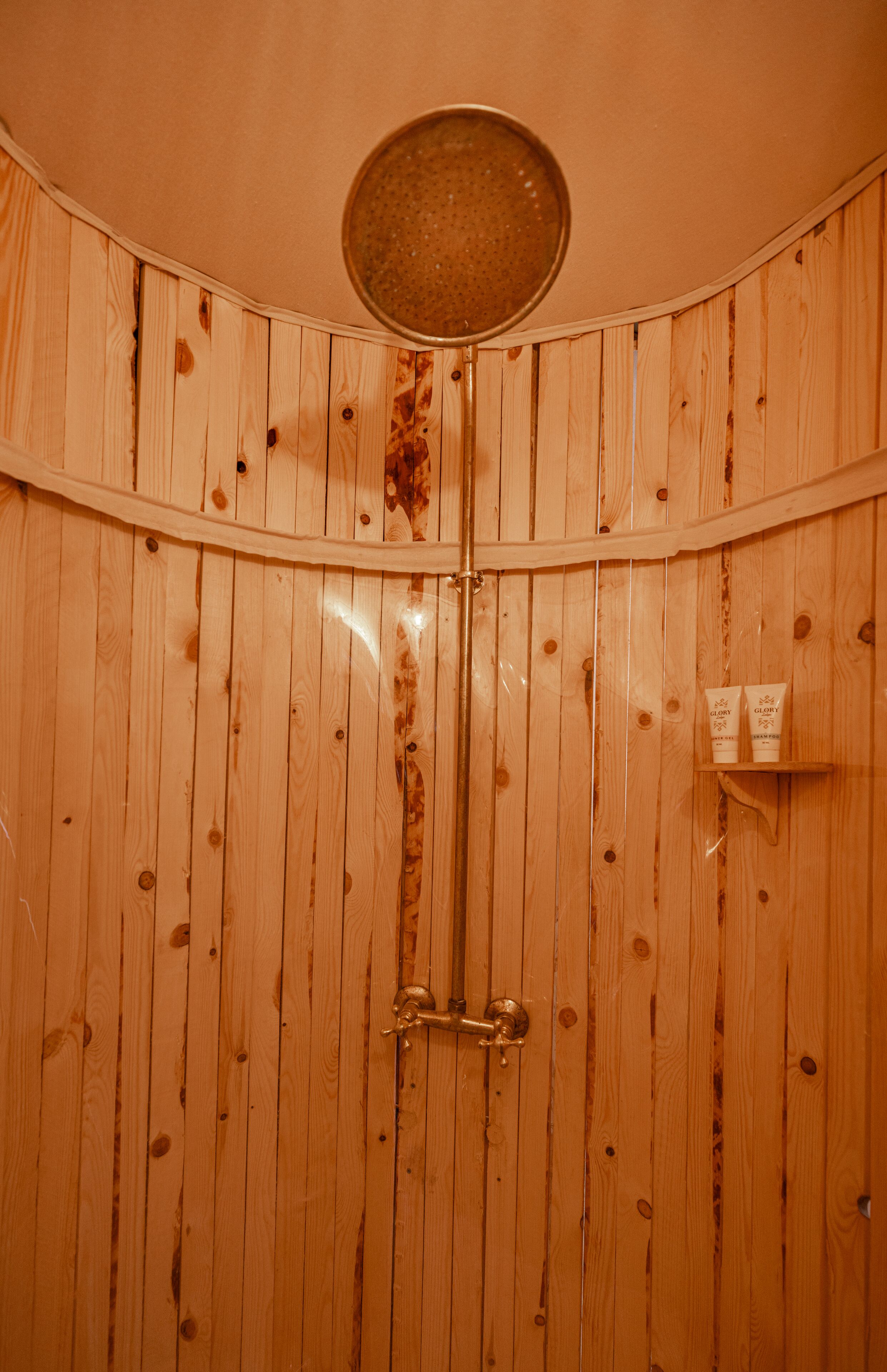 A wooden shower enclosure with a circular showerhead and a small shelf with toiletries.