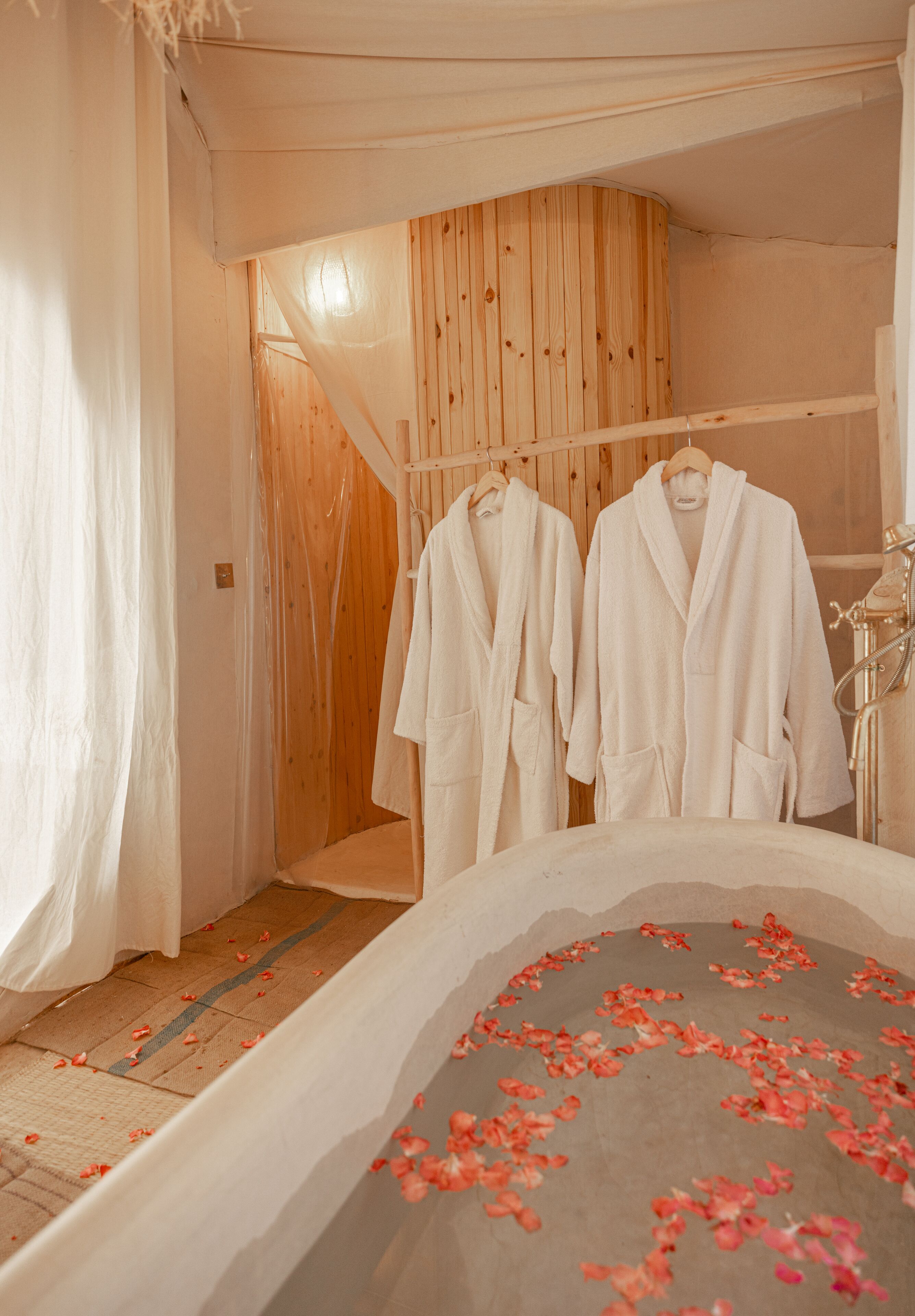 A bathroom with a bathtub, wooden paneling, and two white robes hanging on a rack.