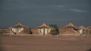 Three thatched-roof huts with large windows, arranged in a row on a sandy terrain. - Imperial Glory Lodges (Rissani)