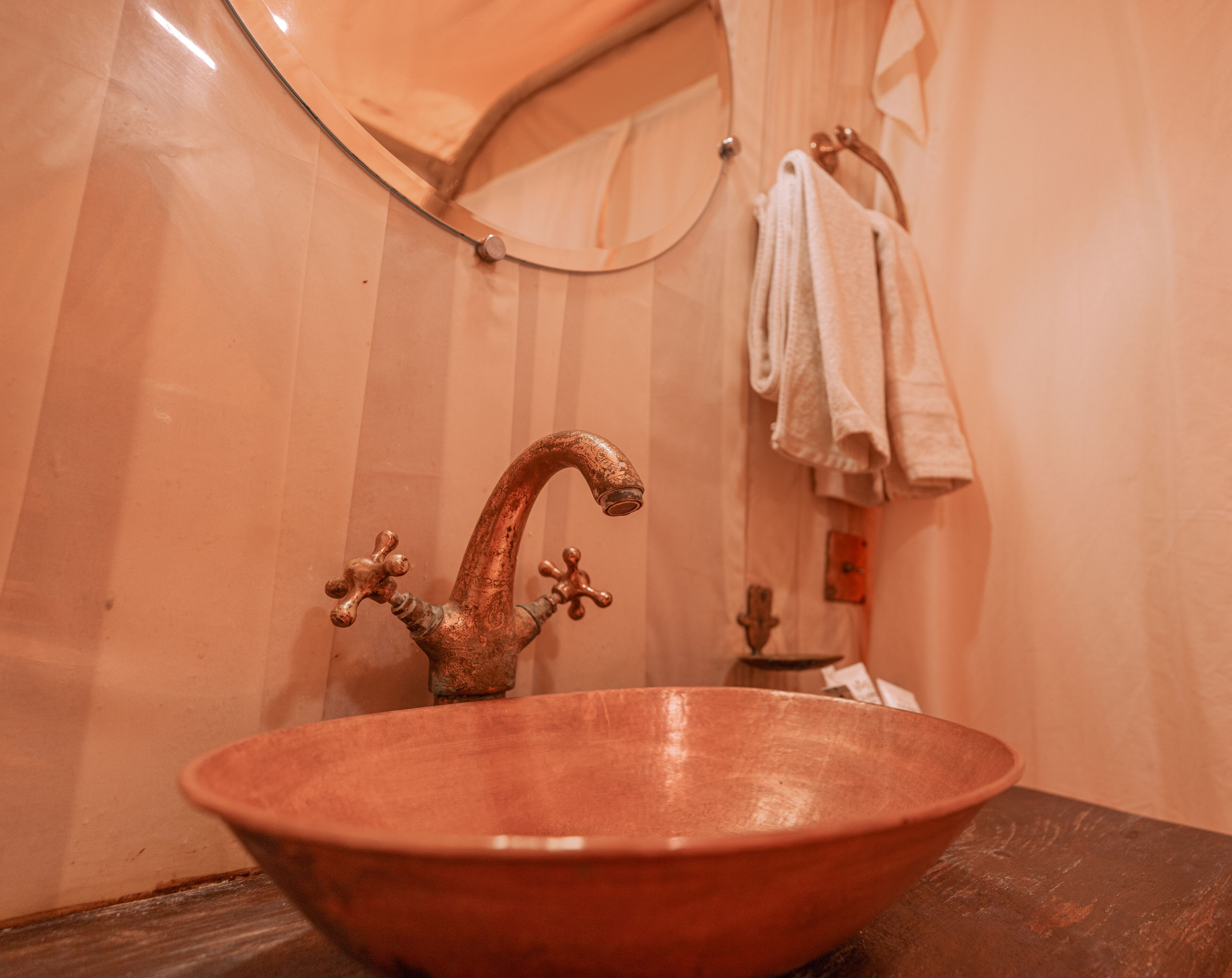Un baño con un lavamanos de cobre, un espejo y un perchero para toallas.