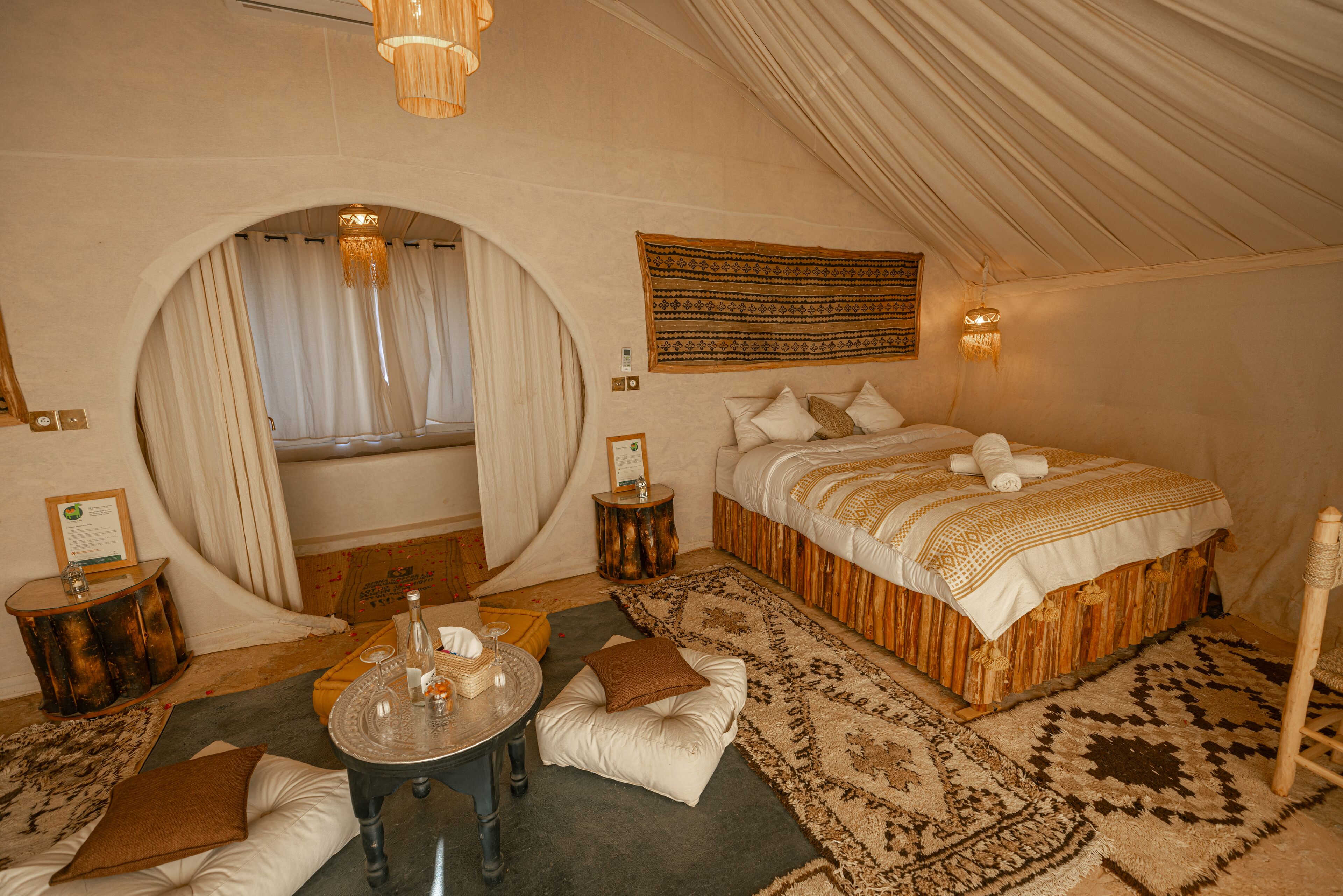 Une chambre confortable avec un grand lit, une table ronde avec des boissons et une fenêtre circulaire originale.