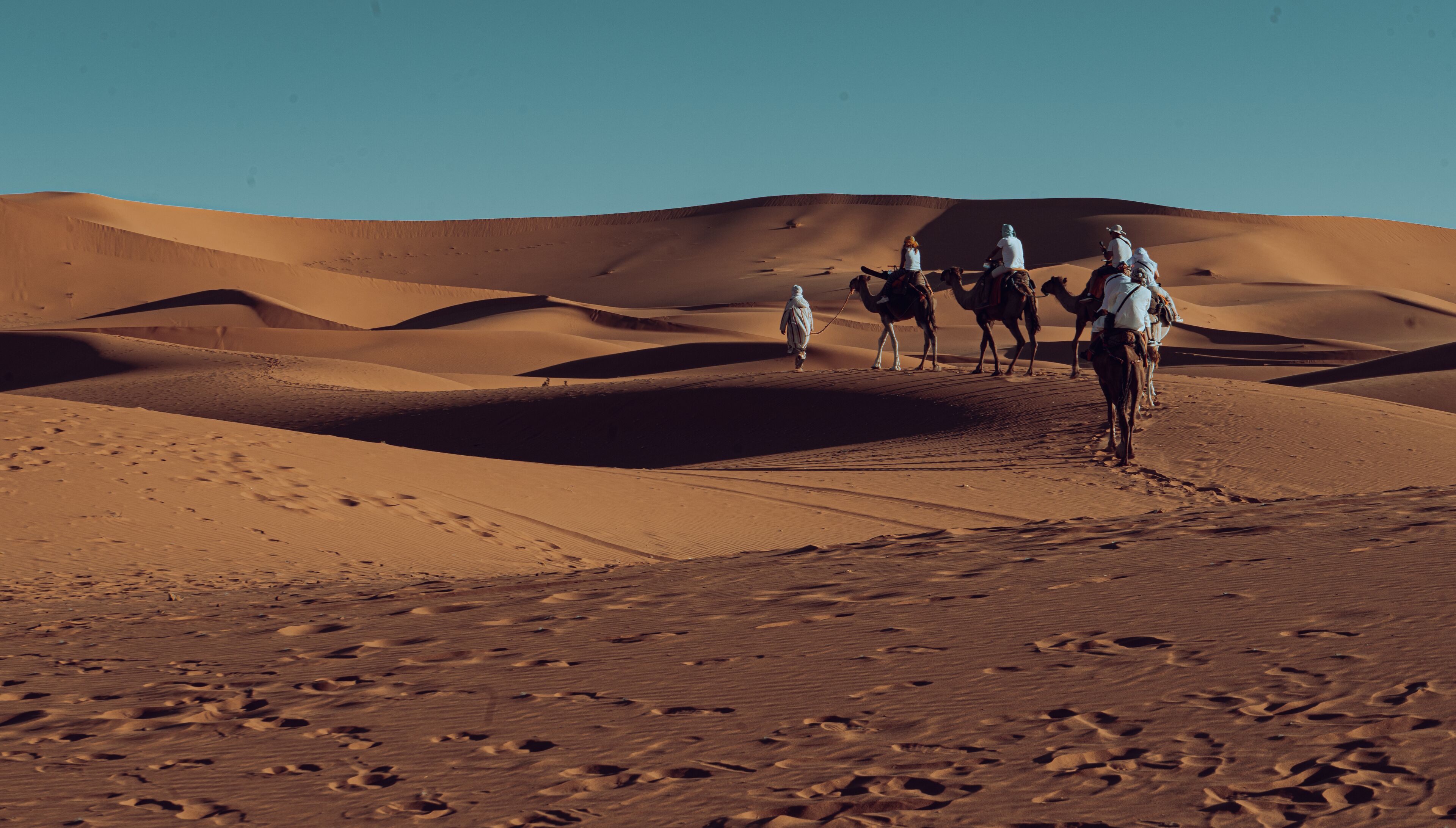 A desert landscape with sand dunes and people riding camels.