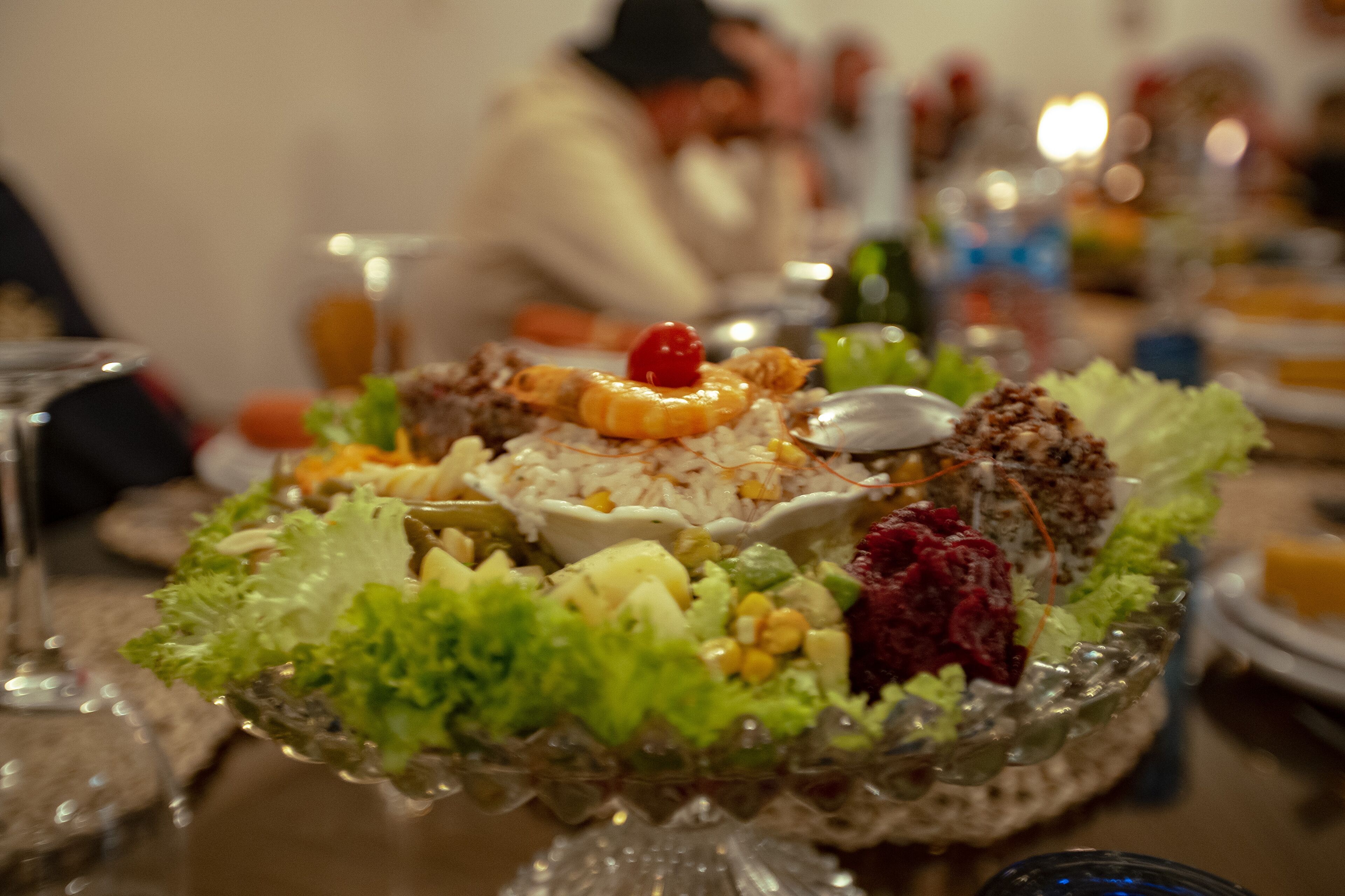 A dining table with a glass bowl containing a salad, a plate with a dessert, and a glass of water.