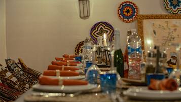 A dining table set with plates, napkins, and various glassware, surrounded by patterned wall hangings and a lantern.