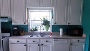 Una cocina con armarios blancos, un fregadero, una cafetera, un microondas y una ventana con una planta.