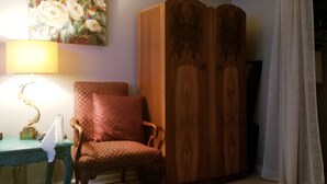Una habitación con un armario de madera, una silla, una mesa con una lámpara y un cuadro en la pared.