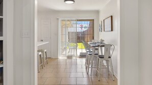 Cozinha iluminada com armários brancos, área de jantar com mesa e cadeiras, e uma porta de vidro deslizante que dá para uma varanda.