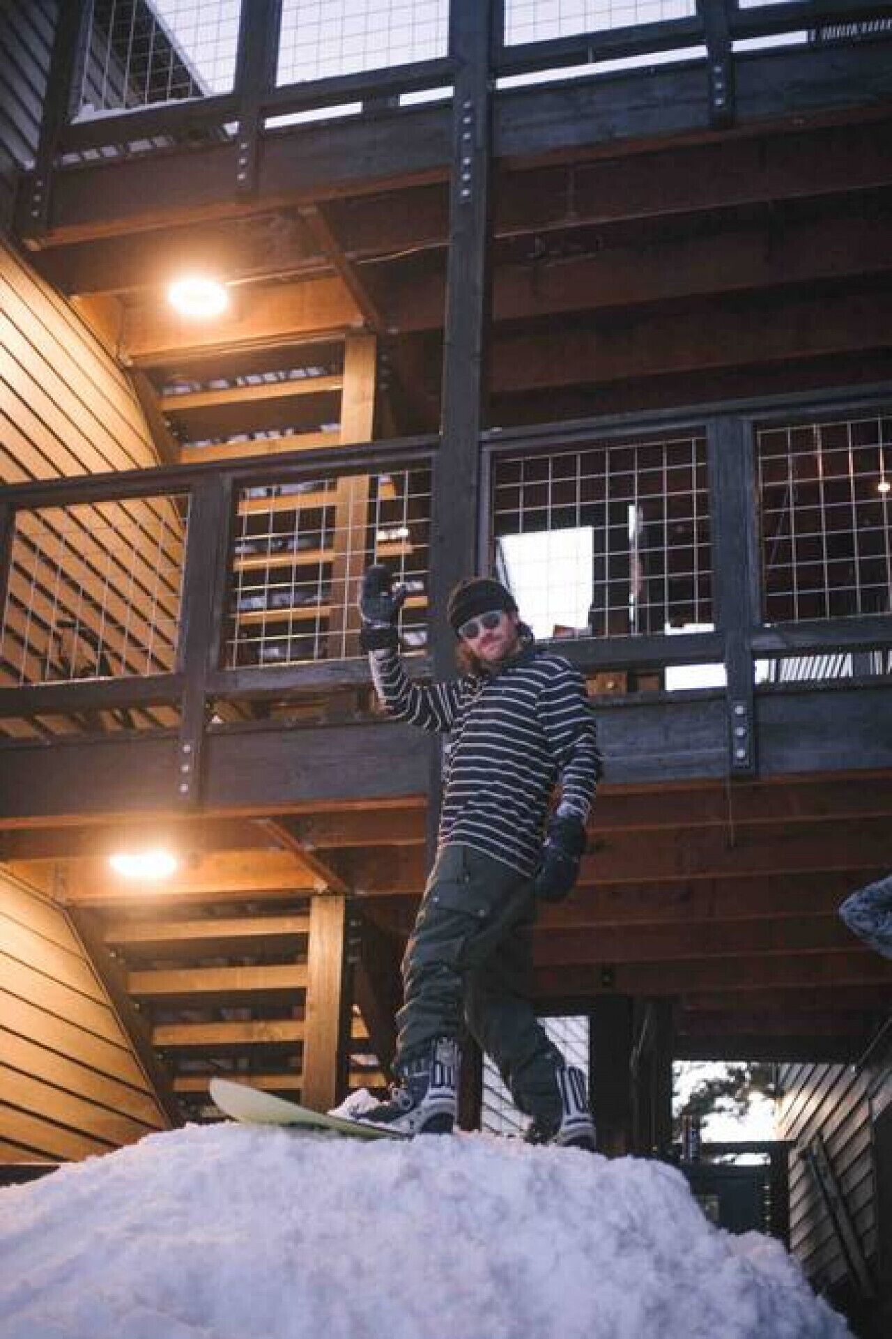 A person standing on a snowboard in front of a building with wooden balconies and large windows.