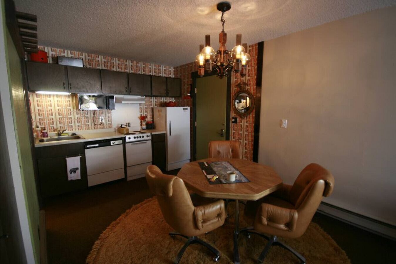 Una cocina compacta con una mesa de comedor y sillas, un refrigerador, estufa y una araña.