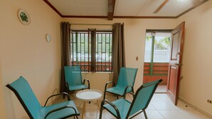 A room with four teal chairs and a small round table, a window with metal bars, and a door leading outside. - Quepos Inn (Quepos)