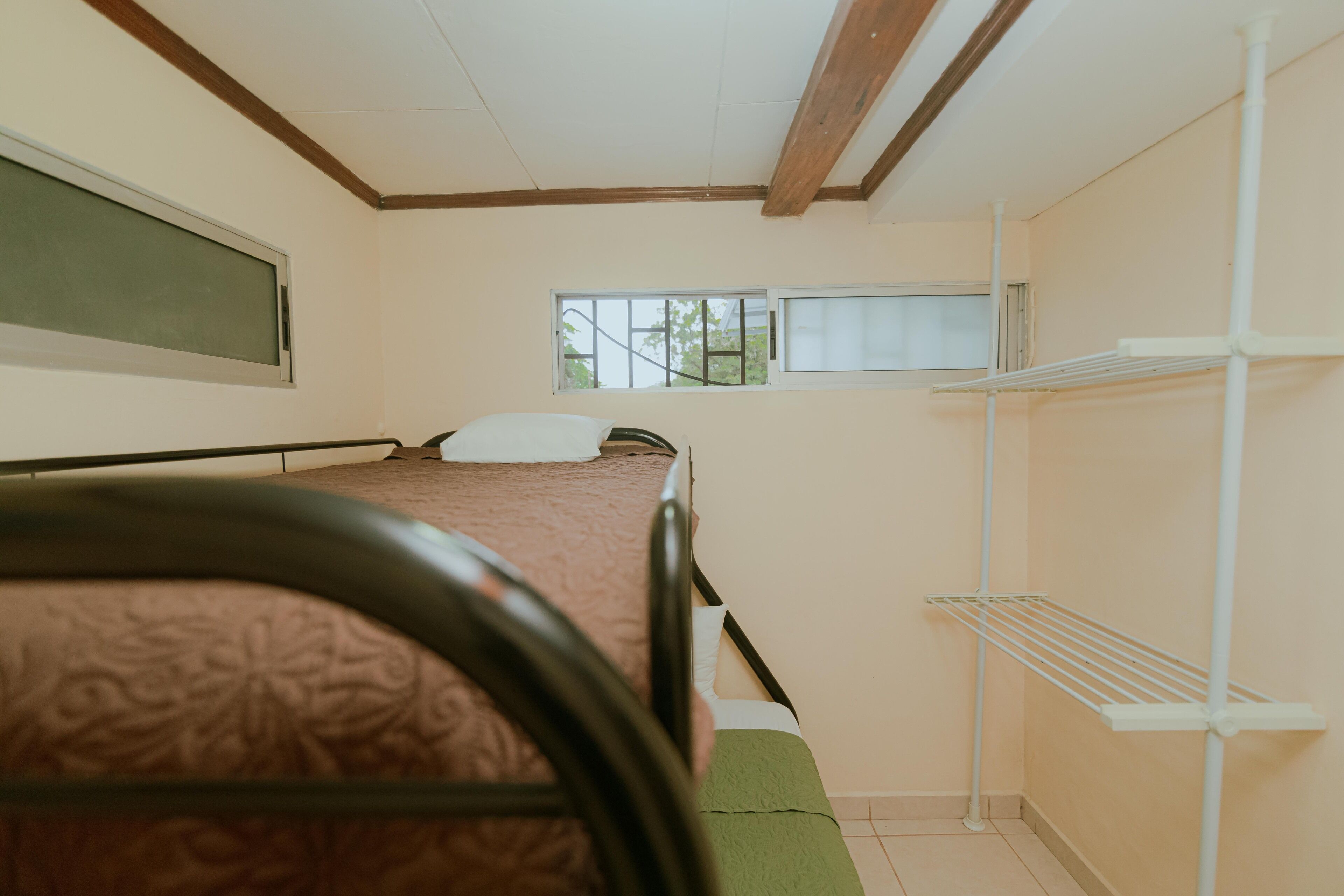 Un lit simple avec une tête de lit, une fenêtre et une étagère blanche dans une pièce au design simple et fonctionnel.