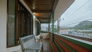 A covered balcony with a bench, a potted plant, and a view of a street with buildings and cars. - Quepos Inn (Quepos)