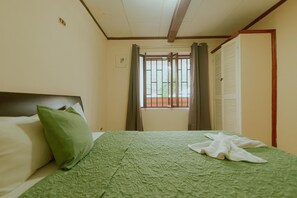 A hotel room with a bed, a window with curtains, and a door.